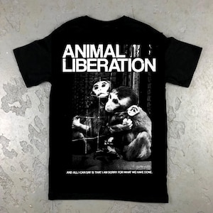 May include: Black t-shirt with a white graphic of two monkeys in a cage. The text "ANIMAL LIBERATION" is printed above the monkeys. The text "AND ALL I CAN SAY IS THAT I AM SORRY FOR WHAT WE HAVE DONE." is printed below the monkeys.