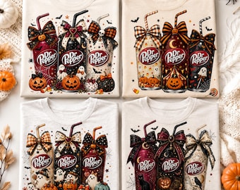 May include: Four light-colored t-shirts featuring graphic prints of Dr Pepper cans decorated for Halloween. Each shirt displays three cans adorned with bows, pumpkins, ghosts, bats, and spiderwebs, with the Dr Pepper logo clearly visible.