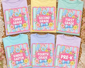 May include: Six short-sleeved t-shirts in pastel colors, each featuring a central graphic of a floral wreath with a blue bow, stars, and text reading THIRD GRADE, SECOND GRADE, FIRST GRADE, KINDERGARTEN, FOURTH GRADE, and PRE-K respectively.