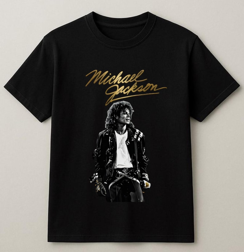 May include: Black t-shirt featuring a gold script of "Michael Jackson" above a black and white image of the singer. The image shows Michael Jackson wearing a black jacket and white shirt.