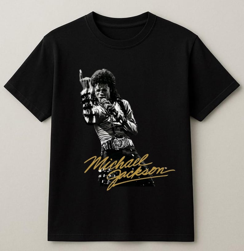 May include: Black t-shirt featuring a black and white image of Michael Jackson performing on stage. The image includes the text "Michael Jackson" in gold script. The shirt is a classic crew neck style.