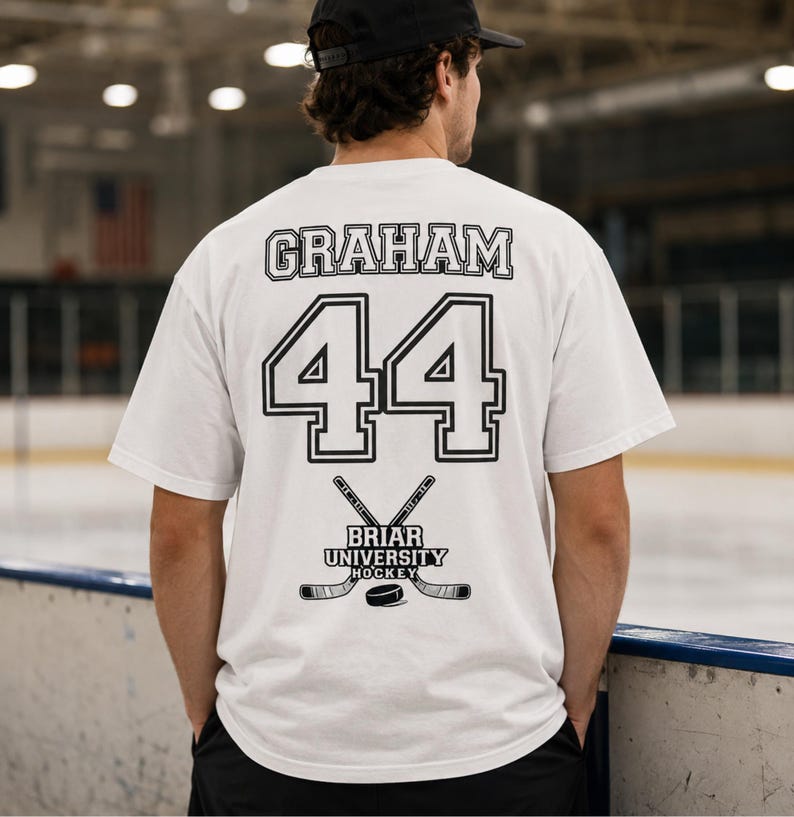 May include: White t-shirt with the name "GRAHAM" above the number "44" in black. Below the number is the text "BRIAR UNIVERSITY HOCKEY" with crossed hockey sticks and a puck. The shirt is short-sleeved.