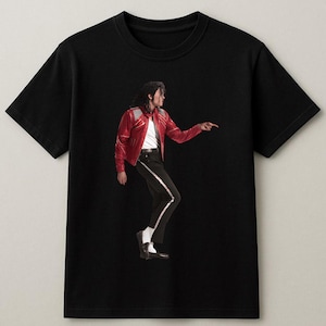 May include: Black t-shirt featuring a full-body image of a person in a red leather jacket, white shirt, black pants with a white stripe, and black shoes. The person is pointing to the right.