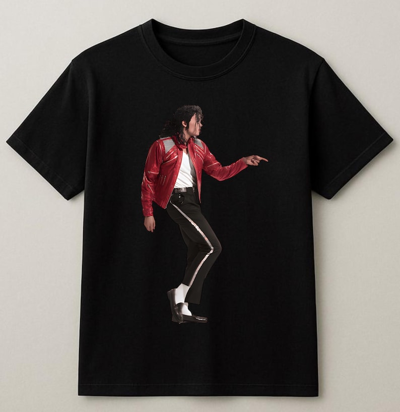 May include: Black t-shirt featuring a full-body image of a person in a red leather jacket, white shirt, black pants with a white stripe, and black shoes. The person is pointing to the right.