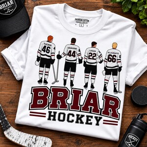 May include: White t-shirt with a hockey team graphic. The shirt features four hockey players with the names and numbers: Tucker 46, Graham 44, Logan 22, and Di Laurentis 66. The text "BRIAR HOCKEY" is displayed in maroon.