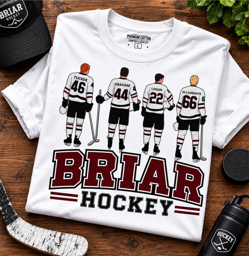 May include: White t-shirt with a hockey team graphic. The shirt features four hockey players with the names and numbers: Tucker 46, Graham 44, Logan 22, and Di Laurentis 66. The text "BRIAR HOCKEY" is displayed in maroon.