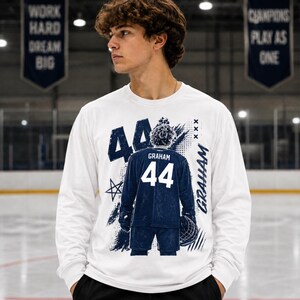 May include: White long-sleeve shirt with a graphic of a hockey player's jersey. The jersey is navy blue with the number 44 and the name "Graham". The shirt has a distressed design with stars and the name "Graham" in a script font.