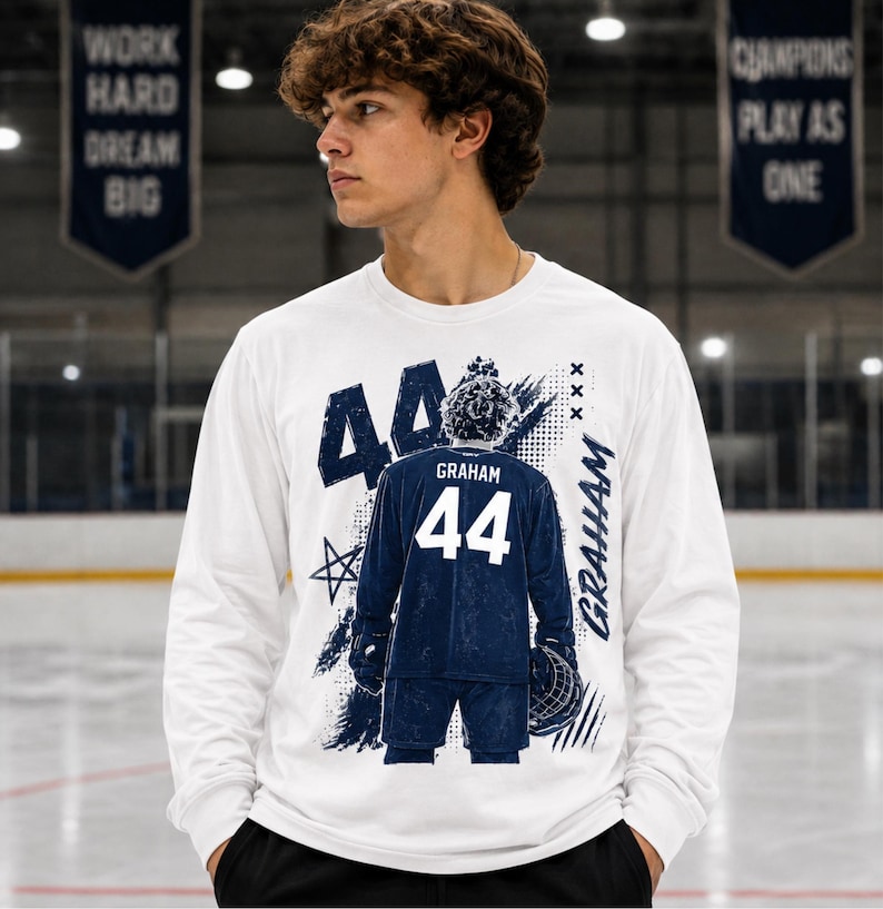 May include: White long-sleeve shirt with a graphic of a hockey player's jersey. The jersey is navy blue with the number 44 and the name "Graham". The shirt has a distressed design with stars and the name "Graham" in a script font.