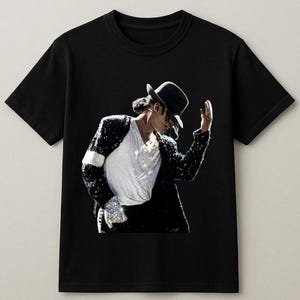 May include: Black t-shirt featuring a graphic of a person wearing a black hat, white shirt, and sequined jacket. The person is in a performance pose. The image is set against a black background.