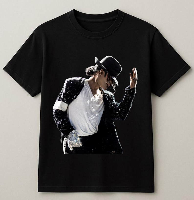 May include: Black t-shirt featuring a graphic of a person wearing a black hat, white shirt, and sequined jacket. The person is in a performance pose. The image is set against a black background.