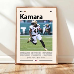 May include: A framed poster featuring a football player in a black and white uniform, holding a football. The poster has the name "Kamara" in large black letters, with the number "41" visible on the player's jersey. The background is a light beige.