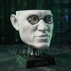 May include: A white bust of a man with black-rimmed glasses, the eyes are hollowed out. The bust is mounted on a black base with the text "THE MATRIX". The bust is a unique decorative item.