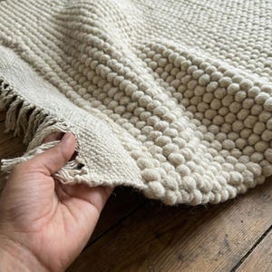 Pode incluir: Tapete texturizado creme com um design de bolhas. O tapete tem formato retangular com borda com franjas. As bolhas criam um efeito tridimensional. O tapete &eacute; feito de um material macio e tecido.