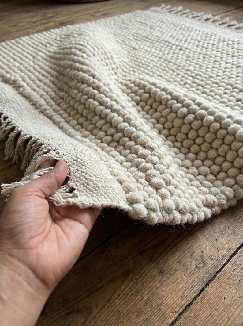 Pode incluir: Tapete texturizado creme com um design de bolhas. O tapete tem formato retangular com borda com franjas. As bolhas criam um efeito tridimensional. O tapete &eacute; feito de um material macio e tecido.