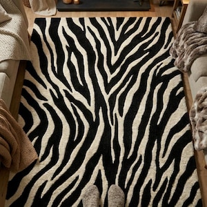 Peut inclure: Un tapis rectangulaire orné d'un motif à rayures zébrées contrastées en noir et blanc cassé. Le tapis présente une construction à poils épais et texturés avec des lignes organiques fluides couvrant toute la surface d'un bord à l'autre.