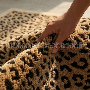 Puede incluir: Una alfombra de felpa color canela con un patrón repetitivo de estampado de leopardo negro. La alfombra tiene un pelo grueso y texturizado y está doblada para mostrar su profundidad. El texto "succesxpobhadohii" aparece en el centro.