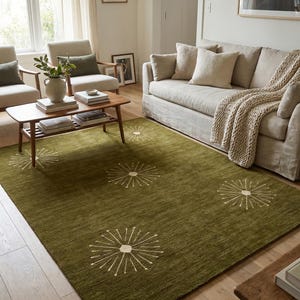 May include: A rectangular area rug in a deep olive green color featuring a repeating pattern of white, starburst-like circular motifs with radiating lines. The rug has a textured, low-pile surface and is positioned on a light-colored wooden floor.