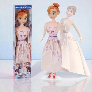 May include: A doll in a box and two other dolls are featured. The dolls have red hair and wear white dresses with purple accents. The box reads "FASHION! CHARM IS INFINITE" and "3+ AGES". The dolls are on a light blue background.