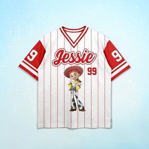 May include: White baseball jersey with red accents, featuring the name "Jessie" in red script and the number "99". The jersey has a cartoon image of Jessie from Toy Story. The sleeves are red with white stripes.