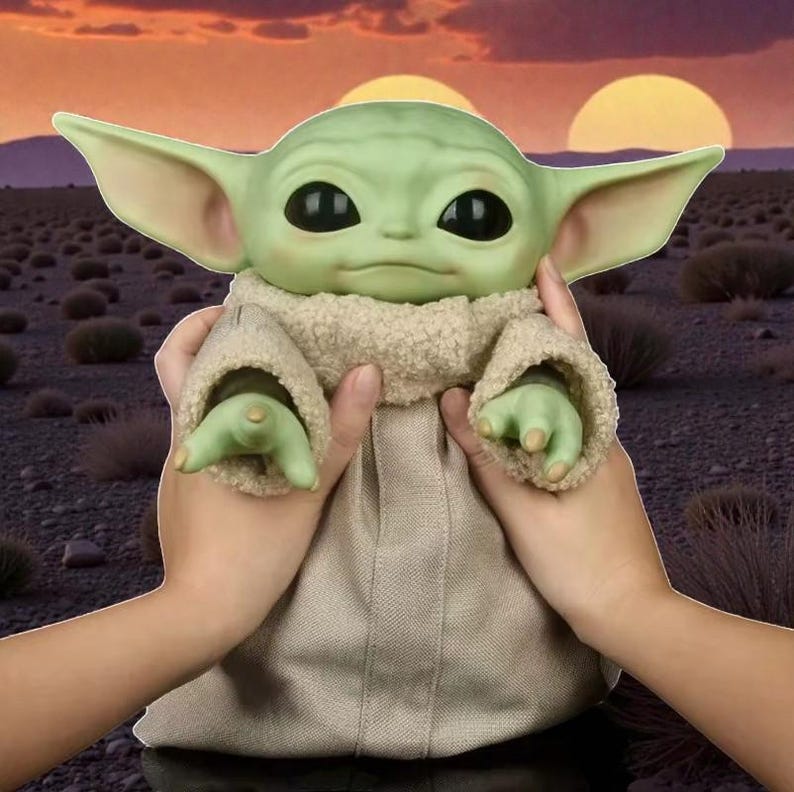 May include: A green-skinned doll with large ears and black eyes, wearing a tan robe and held by two hands. The background features a desert landscape with two suns setting in a colorful sky.