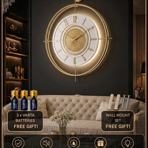 Op de afbeelding: Een ronde wandklok met een gouden metalen frame, een witte wijzerplaat met gouden Romeinse cijfers en een centraal goudkleurig geometrisch patroon. De set bevat drie Varta-batterijen en een wandmontageset, met vermeldingen van een geruisloos uurwerk en roestvrije metalen constructie.
