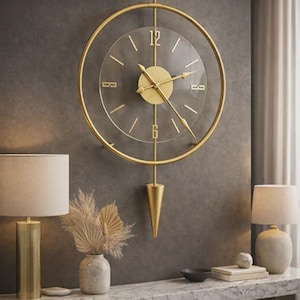 May include: A gold-colored, circular wall clock with a clear face and gold hands. The clock has a pendulum and is mounted on a dark gray wall. The clock is part of a home decor theme.