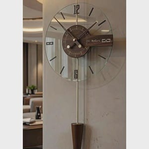 Könnte beinhalten: Eine moderne Wanduhr mit transparentem Zifferblatt und dunklem Holzmittelpunkt. Die Uhr hat schwarze Zeiger und Stundenmarkierungen, mit einem Pendel und einem Holzgewicht. Die Uhr ist an einer hellen Wand befestigt.