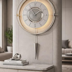 May include: A silver and gold-toned wall clock with Roman numerals and a pendulum. The clock has a circular design with a light-coloured face and a decorative, geometric centre. The clock is mounted on a light grey wall.