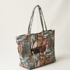 May include: A large tote bag with a patchwork design. The bag features a mix of denim and brown leather-like patches. The handles and body of the bag are in shades of grey, brown, and blue. The bag is designed for carrying items.