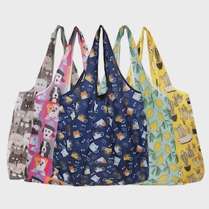 May include: A selection of reusable shopping bags featuring diverse patterns. Designs include cats, dogs, lemons, and cacti. The bags are in shades of grey, pink, blue, green, and yellow. Each bag has a matching handle.