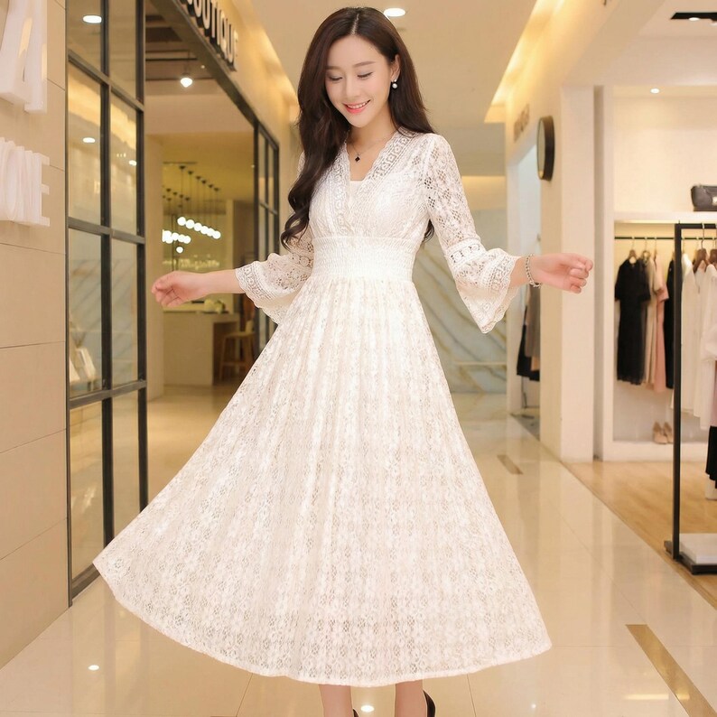 Puede incluir: Un vestido de encaje blanco con escote en V y mangas largas acampanadas. El vestido tiene una cintura ajustada y una falda fluida. El vestido est&aacute; hecho de una delicada tela de encaje y es adecuado para ocasiones especiales.