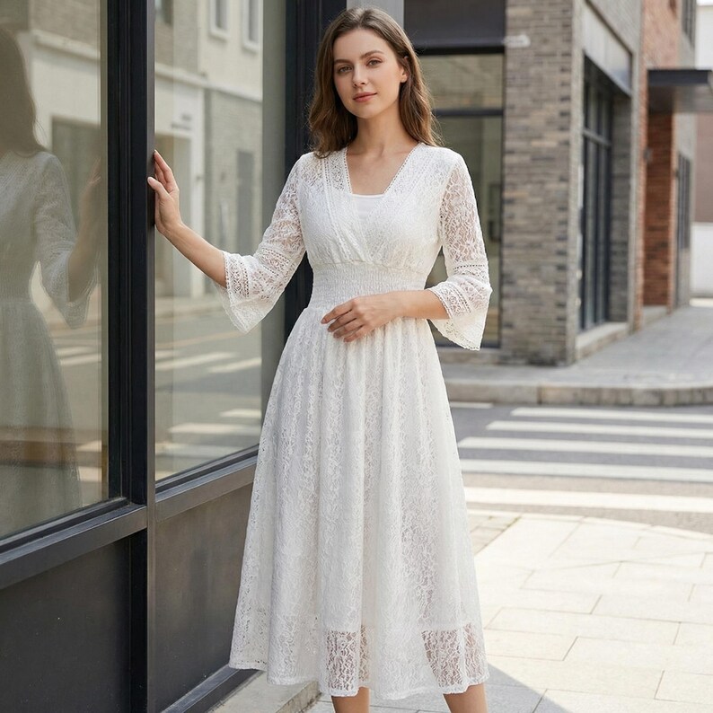 Puede incluir: Vestido blanco de encaje con escote en V y mangas tres cuartos. El vestido presenta un corpi&ntilde;o ajustado y una falda fluida, creando una silueta elegante. Las mangas tienen un dise&ntilde;o acampanado y el vestido llega a media pantorrilla.