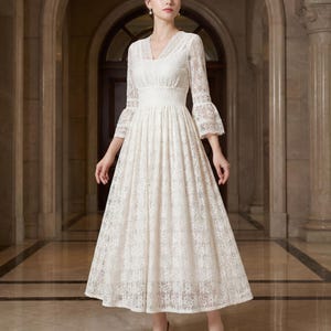 Puede incluir: Un vestido de encaje color crema con escote en V y mangas tres cuartos. El vestido presenta un corpi&ntilde;o ajustado y una falda acampanada, creando una silueta elegante. Las mangas tienen forma de campana en los pu&ntilde;os. El vestido es adecuado para eventos formales.