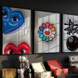 May include: Three framed wall art prints featuring a blue heart with eyes, a red heart with eyes, a colorful rainbow flower with a smiling face, and a black Stussy logo above a black eight ball, displayed in a room with various collectible figures.