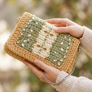 May include: A rectangular crochet clutch bag featuring a tan border and a central panel with alternating vertical stripes of sage green and cream yarn. The surface is embellished with clear, amber, and light green faceted crystals and beads.