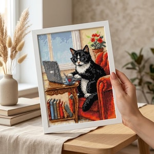 Può includere: Un diamond painting incorniciato raffigurante un gatto bianco e nero con occhiali, seduto su una poltrona rossa davanti a una scrivania in legno con un portatile e una tazza. Sotto la scrivania si vede una fila di libri colorati e una pianta.