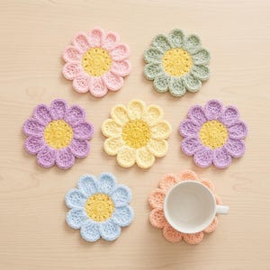 May include: A collection of handmade crochet flower coasters in various pastel colors, including pink, yellow, purple, blue, and green. One coaster holds a white teacup. The coasters have a yellow center and petal-shaped edges.