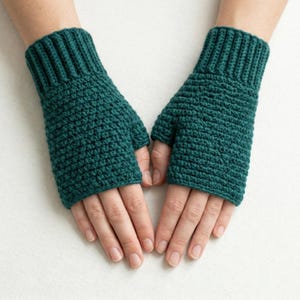May include: Teal fingerless gloves, hand-knitted with a textured stitch. The gloves have a ribbed cuff and cover the hand up to the knuckles, leaving the fingers exposed. The gloves are displayed on a white surface.
