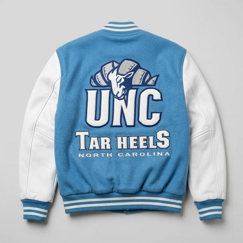 Puede incluir: Una chaqueta universitaria azul claro con mangas blancas y ribetes a rayas. La parte posterior presenta un gran gr&aacute;fico bordado de una cabeza de carnero sobre el texto UNC, Tar Heels y North Carolina en letras blancas y azul marino.