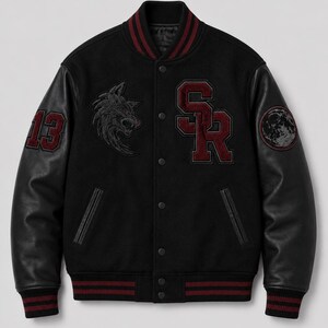 May include: A black varsity jacket with black leather sleeves and a snap-button front. The chest features a wolf head embroidery, the letters SR in maroon, and the number 13 on the right sleeve. A circular moon patch is on the left sleeve.