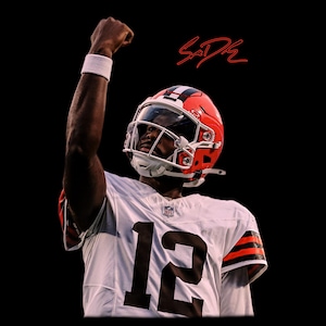 May include: A football player in a white and brown uniform with the number 12, raising a fist in celebration. The player wears a brown and white helmet with a clear visor. The background is black, with a red signature.