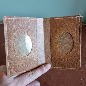 Puede incluir: Cartera marr&oacute;n hecha a mano, abierta para revelar dos recortes ovalados. La cartera est&aacute; hecha de un material texturizado similar al papel con costuras visibles. El interior presenta una franja marr&oacute;n m&aacute;s clara.
