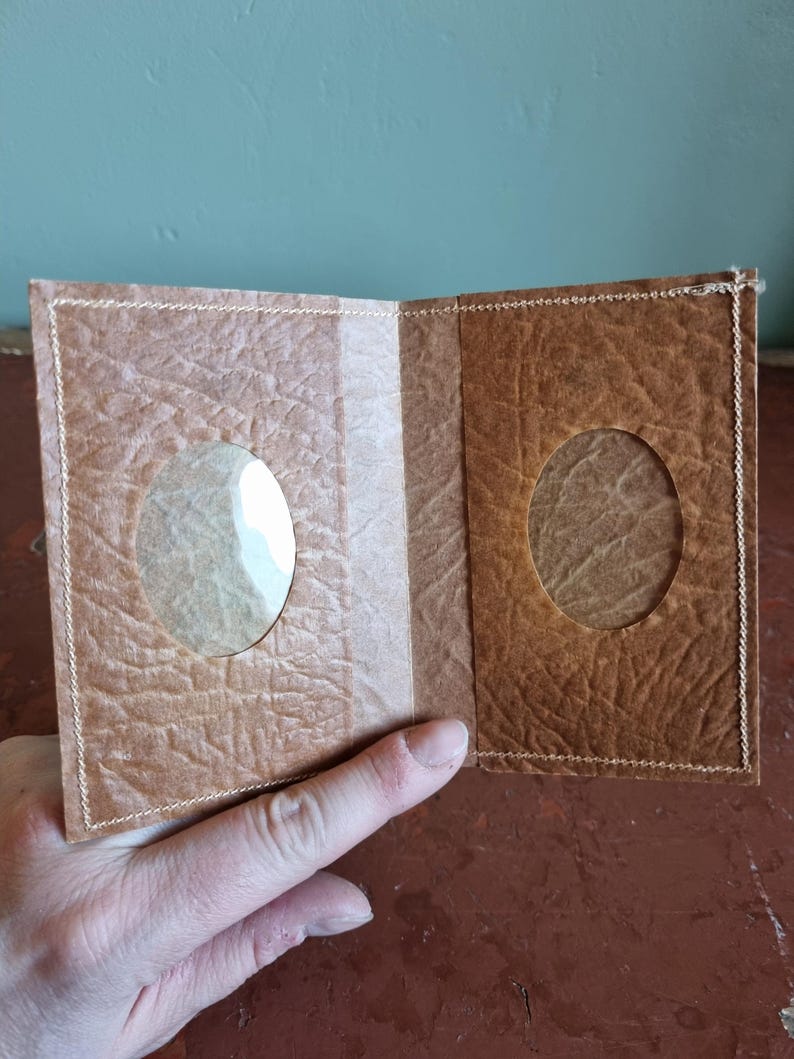 Puede incluir: Cartera marr&oacute;n hecha a mano, abierta para revelar dos recortes ovalados. La cartera est&aacute; hecha de un material texturizado similar al papel con costuras visibles. El interior presenta una franja marr&oacute;n m&aacute;s clara.