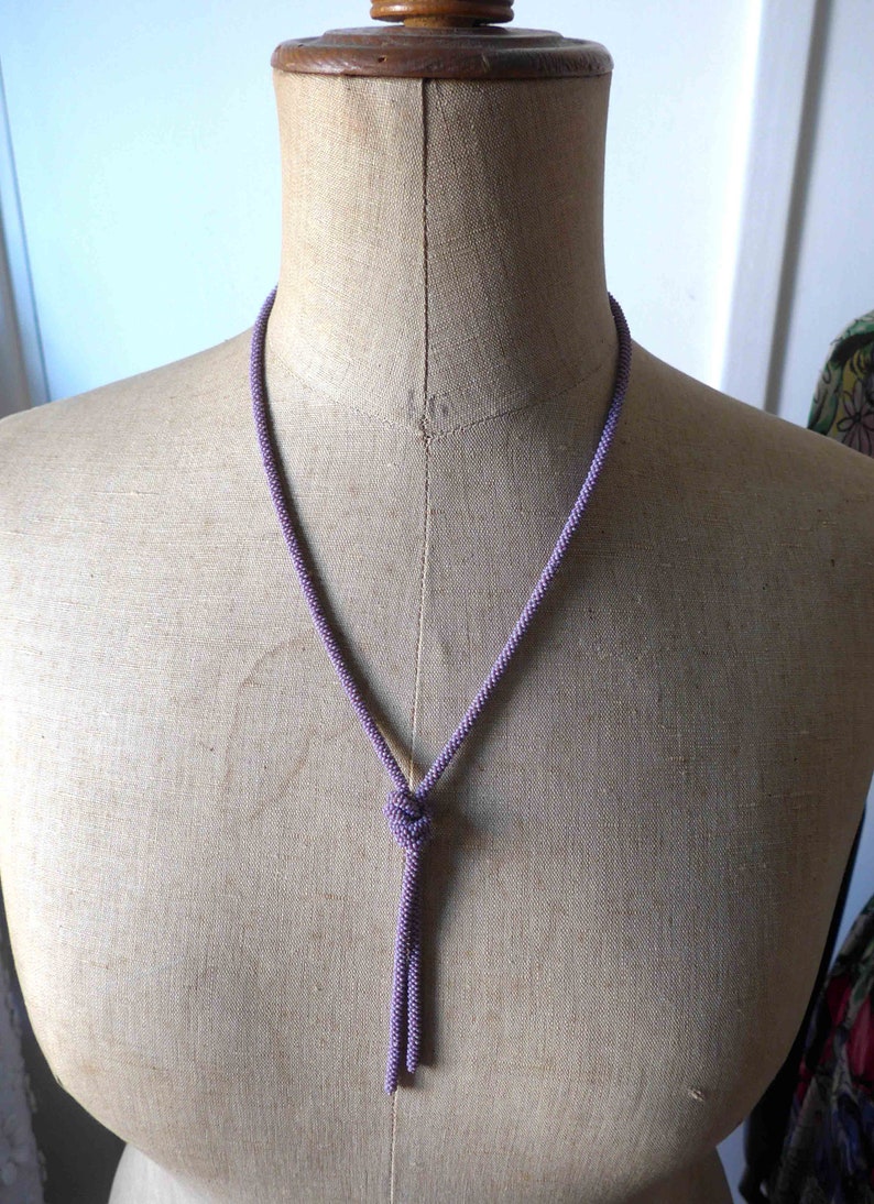 Pu&ograve; includere: Una collana di perline viola con un pendente annodato &egrave; appesa a un manichino.