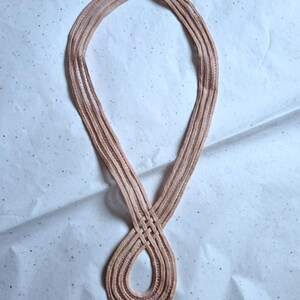 Peut inclure: Un collier marron clair avec un motif tiss&eacute;. Le collier est fait d'un mat&eacute;riau souple et flexible et est en forme de huit. Le fond est une surface blanche avec de petits paillettes &eacute;parpill&eacute;es.