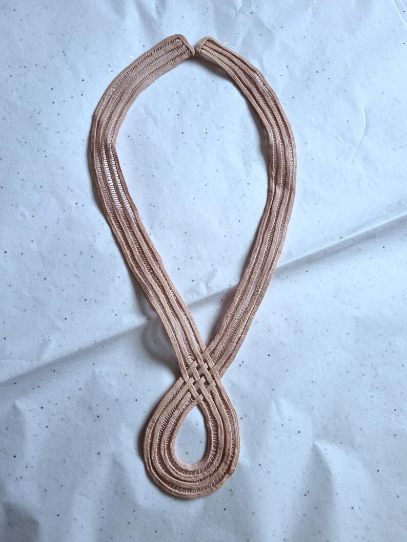 Peut inclure: Un collier marron clair avec un motif tiss&eacute;. Le collier est fait d'un mat&eacute;riau souple et flexible et est en forme de huit. Le fond est une surface blanche avec de petits paillettes &eacute;parpill&eacute;es.