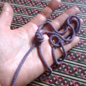 Pu&ograve; includere: Una lunga e sottile collana di perline viola con un designo annodato. La collana &egrave; fatta di piccole perline rotonde e si trova su una mano.