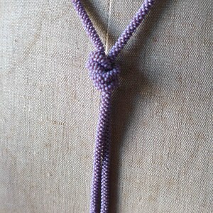Pu&ograve; includere: Una collana lunga e sottile fatta di piccole perline viola. La collana &egrave; annodata in cima e pende in due fili.
