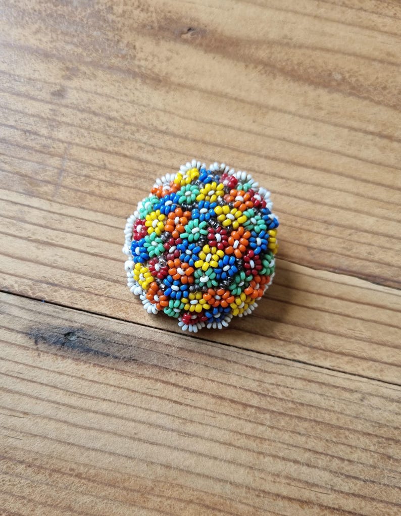 May include: A colorful beaded brooch with a floral design. The brooch is made of small, round beads in shades of red, orange, yellow, green, blue, and white.