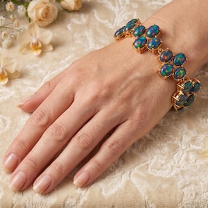 May include: A gold link bracelet featuring multiple oval-shaped dark blue opals with iridescent flashes of green and red. The bracelet is constructed with a series of connected settings, each holding a polished, smooth, dark blue gemstone.